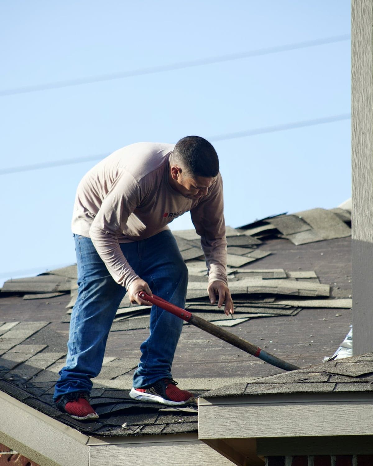 Roofer tearing old shingles off a residential roof